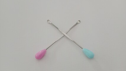 Two ear picks, one pink and one blue, crossed on a white background