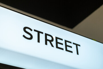 Close-up side angle of an illuminated white retail sign with the word "STREET" above a footwear display in a modern store interior.