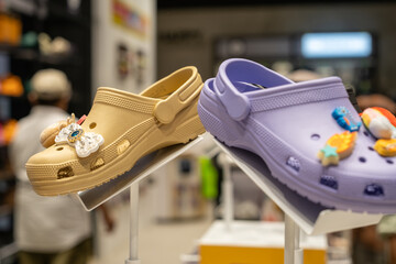 Close-up of stylish rubber clogs with playful decorative charms on display at a fashion retail store. Beige and purple footwear stand out in a trendy indoor shopping environment.