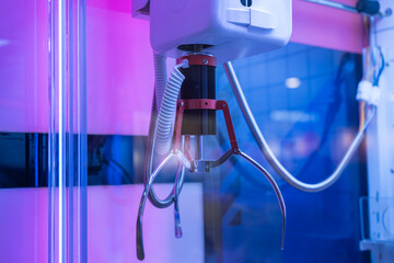 Close-up of a claw machine gripper inside an arcade game with vivid blue and purple neon lighting, showing mechanical details and vibrant reflections.