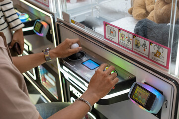A person operating a claw machine with joystick and button controls, aiming to win plush toys....