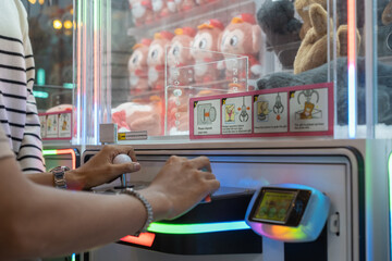 Hands operating a joystick and button on a claw machine at an arcade, with colorful plush toys and instruction stickers in the background.