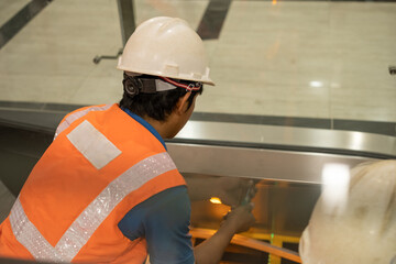 A worker wearing safety gear repairing an escalator in a building, focused on maintenance with protective equipment and tools.