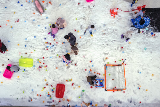 Top view of children playing in artificial snow with colorful balls and toy soccer nets indoors, depicting cheerful winter fun, family bonding, and interactive kids' playground activities.