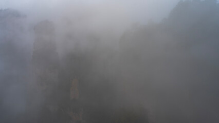 A mystical misty landscape. The high pillars mountains are shrouded in thick fog. The outlines of the rocks are barely visible through the haze. Poor visibility. China.Zhangjiajie National Forest Park