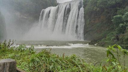 Beautiful tropical waterfall. Streams of white water flow down from a sheer cliff into the riverbed. Splashes, fog. Foam on river rapids. Green vegetation. China. Huangguoshu Waterfall. Guizhou