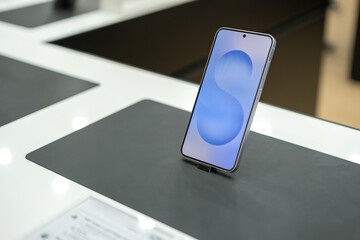 Close-up of a Samsung Galaxy S24 or s25 smartphone displayed upright on a demo counter with a glowing screen, highlighting its sleek design and modern user interface.
