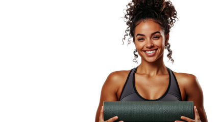 A fit and athletic woman wearing a sports tank top stands holding a rolled up yoga mat smiling at the camera, isolated on a transparent background. PNG