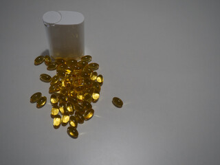 A group of capsules spilled next to a white plastic container on a plain background, highlighting...