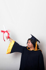Young brunette Latina woman dressed in a cap and gown shows her diploma proudly, satisfied and...
