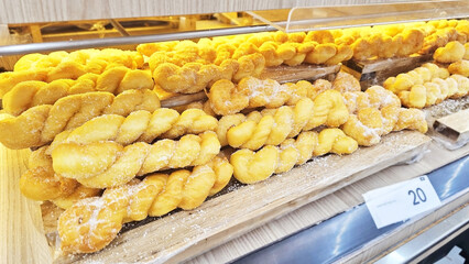 Sugar Twisted Doughnut Delights: A tempting close-up of rows of freshly baked, twisted doughnuts artfully arranged in a bakery display, enticing with their golden-brown hue and sugared finish.