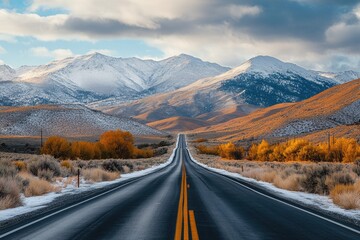 A paved road stretches into a mountain range,  golden fall foliage,  and a wintery vista