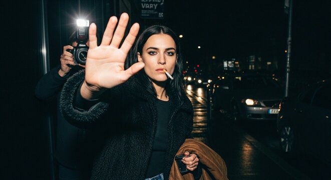 Night time photo of a female model celebrity smoking a cigarette, one hand up trying to stop paparazzi from taking a picture,  privacy, urban, city night, street lights, candid, attitude, edgy, glam