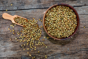 Spice coriander (Coriandrum sativum) seeds in wooden bowl and spoon on wooden background. Indian...