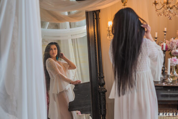 A brunette woman stands quietly in the morning light, wrapped in a sheer white vintage gown, ...