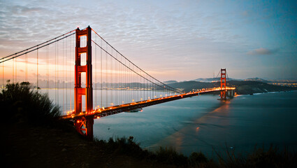 Obraz premium Golden Gate at Night: A Stunning View of the Iconic Bridge, City Lights and Calm Ocean Reflections