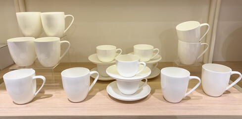 A row of white cups and saucers are displayed on a wooden shelf