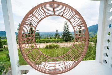 Circular woven hanging chair on a patio with a scenic view of pine trees and rolling hills in the...