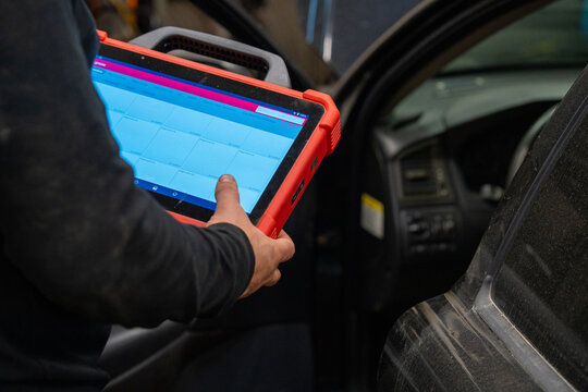 A Car diagnostic specialist using an electronic tablet scanner in an automotive repair garage. Mechanic performing vehicle computer system analysis with professional diagnostic equipment