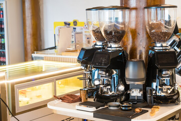 Three commercial coffee grinders with coffee beans in a cafe setting next to espresso maker and accessories.