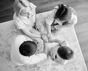 Top view of family holding each others wrists in circle. Four members of family holding hands linked in lock against light background. Parents showing to kids their support. Black and white image.