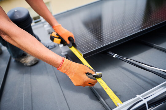Worker building solar panel system on rooftop of house for generating electricity through photovoltaic effect. Close up man using ruler to measure mounting equipment for precise installation.