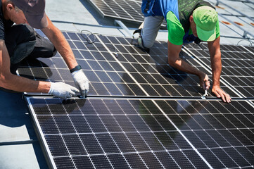Workers building photovoltaic solar panel system on rooftop of house. Men engineers installing...