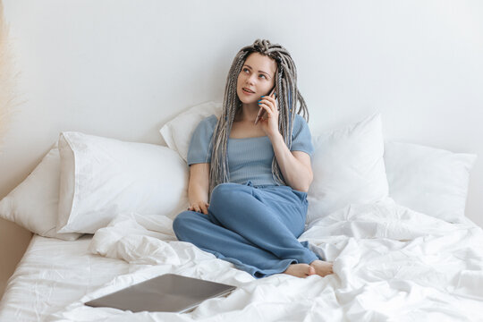 Young woman talking on the phone in white bed.