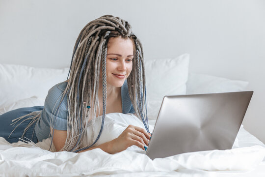 Young woman communicating at laptop in white bed.