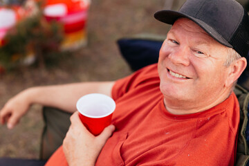 Smiling man with red cup relaxing in outdoor camping chair