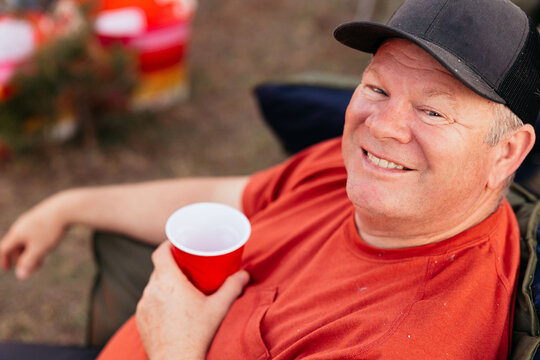 Smiling man with red cup relaxing in outdoor camping chair