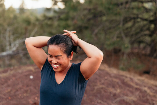 Smiling Thai woman outdoors tying hair into ponytail while camping