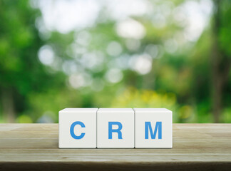 CRM acronym on white block cubes on wooden table over blur green tree in park, Customer...