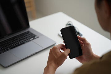 Person using smartphone at desk with laptop in minimalist workspace