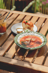 Delicious Ukrainian borscht with pear, bread and drinks served on a wooden table.