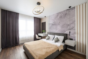 Modern bedroom with a gray bed, textured wall, stylish lighting, dark curtains, and a sleek vanity...