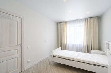 minimalist bedroom features a white bed, light wood floors, and neutral curtains. The room is bathed in natural light, creating a serene atmosphere