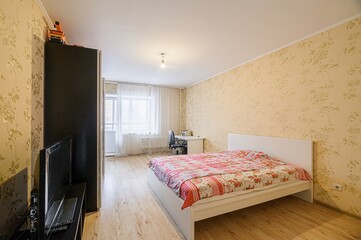 cozy bedroom featuring a bed with a floral quilt, a desk near the window, and a black wardrobe. The...