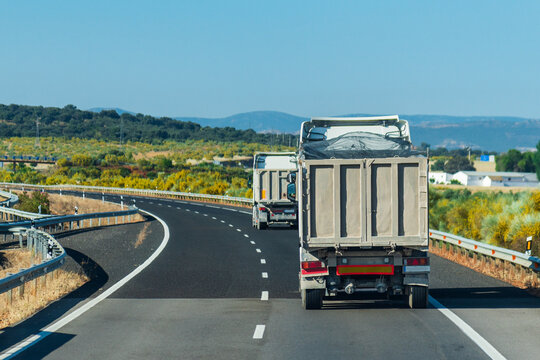 Two trucks with tipping semi-trailers for transporting aggregates driving on a highway.
