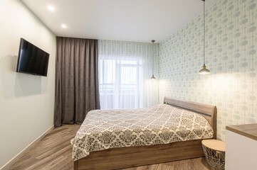 cozy bedroom with a wooden bed, patterned bedding, and hanging lamps. There's a TV on the wall,...