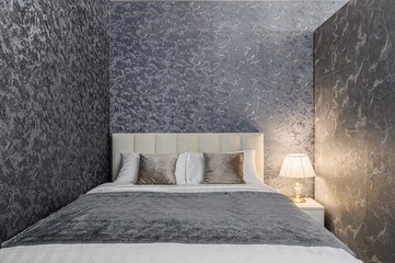 cozy bedroom featuring a plush bed with textured walls, soft pillows, and a warm bedside lamp