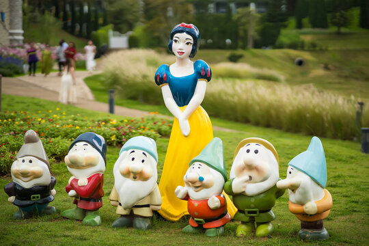 Colorful sculptures of Snow White and the Seven Dwarfs standing in a lush, green garden setting with a blurred background
