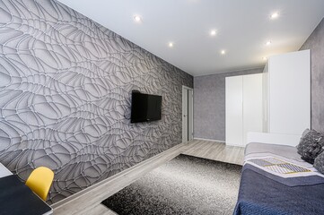 modern room featuring a patterned wallpaper wall with a TV, a wardrobe, and a bed with a gray and...