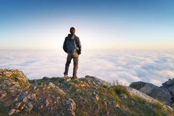 Man stands over the cover clouds on the edge of the abyss and looks on sun.
