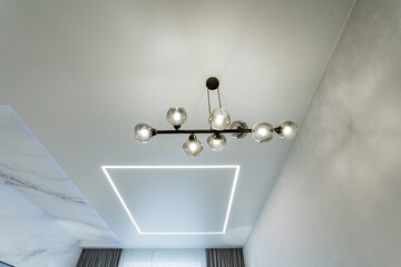 The bedroom showcases a perfectly square ceiling adorned with an elegant chandelier that gracefully...