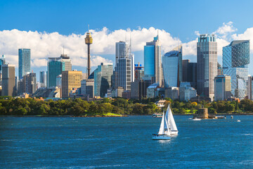 Beautiful Sydney city skyline panorama with tower and modern skyscrapers viewed across the harbour from Bradleys Head with blue sky and white fluffy clouds on a day