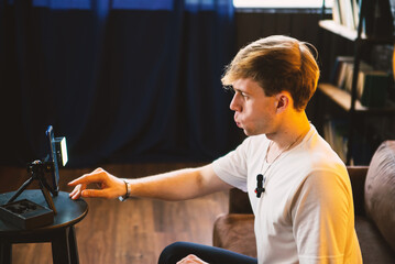Young man touches smartphone screen with cheeks puffed, using a tripod and light for online...