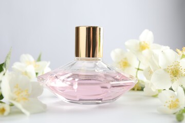 Bottle of perfume and jasmine flowers on white table, closeup
