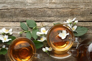 Aromatic jasmine tea in glass cups, teapot, flowers and green leaves on wooden table, flat lay