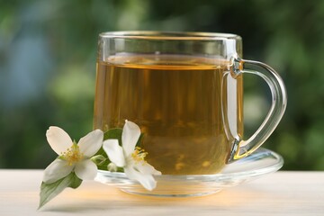 Tasty jasmine tea in cup and flowers at white wooden table, closeup
